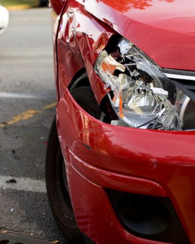 A red car with a damaged headlight after an accident