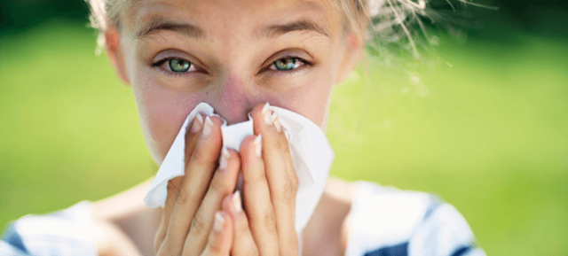 woman blowing nose from allergy symptoms