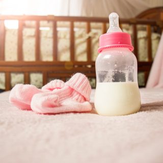 Pink baby booties and bottle of formula with crib