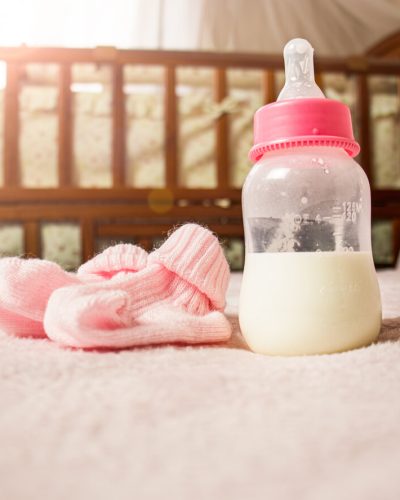 Pink baby booties and bottle of formula with crib