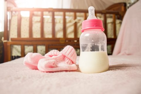 Pink baby booties and bottle of formula with crib