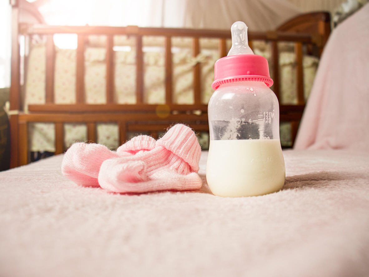 Pink baby booties and bottle of formula with crib