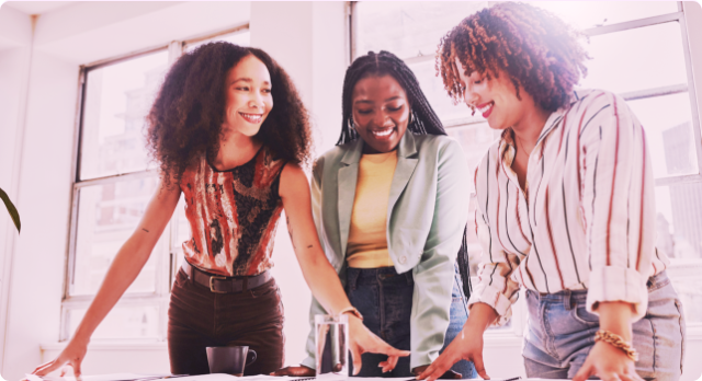 Three professional black women in the workplace collaborating on a project