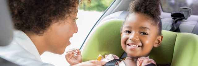 Mother buckling her daughter into a car seat