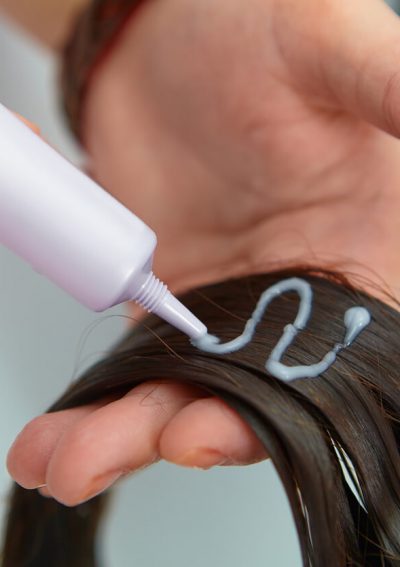 Woman applying chemical hair straightener to her hair.