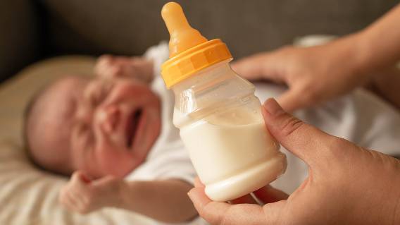 Crying baby with bottle of formula