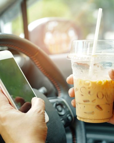 Person with phone and coffee in hand while driving