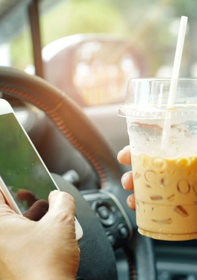 Person with phone and coffee in hand while driving