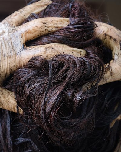 Close-up of dye-stained gloves massaging dark hair dye into wet strands during a coloring treatment.
