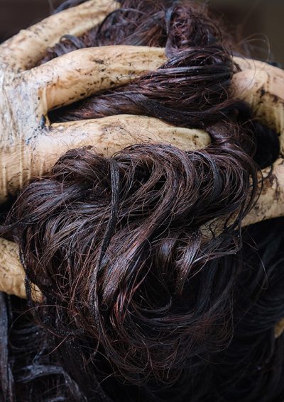 Close-up of dye-stained gloves massaging dark hair dye into wet strands during a coloring treatment.