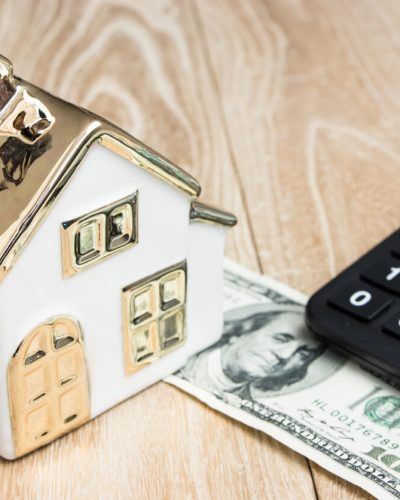 House model with money and a calculator in front of a wood background