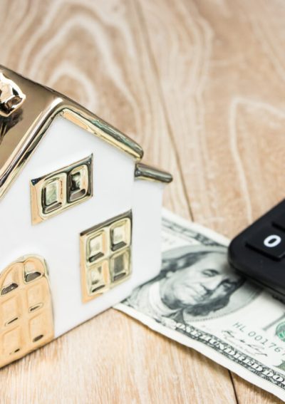 House model with money and a calculator in front of a wood background