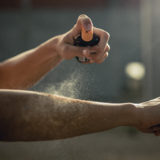 Person spraying aerosol sunscreen on their arm