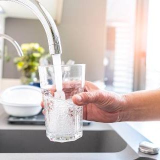 Woman with glass getting water from tap