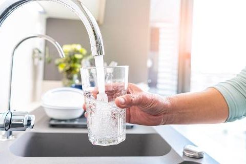 Woman with glass getting water from tap