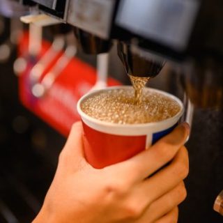 Hand with cup held up to soda dispenser