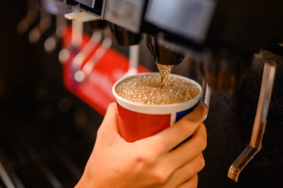 Hand with cup held up to soda dispenser