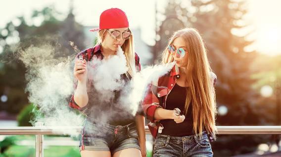 Two teen girls vaping outdoors