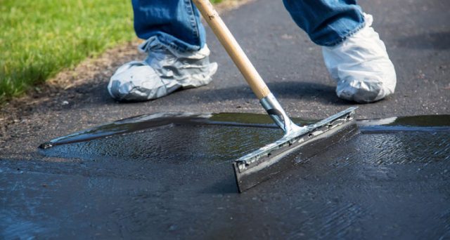 Worker spreading coal tar-based sealant on a driveway